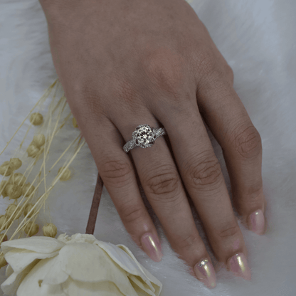 Hand wearing a silver ring with a diamond on a white background with flowers.