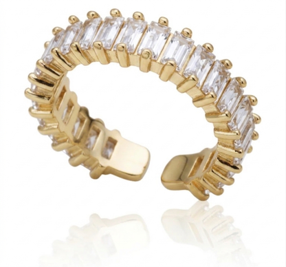 A gold-plated adjustable ring band featuring a row of clear rectangular baguette-cut gemstones, shown on a white background with a soft reflection.