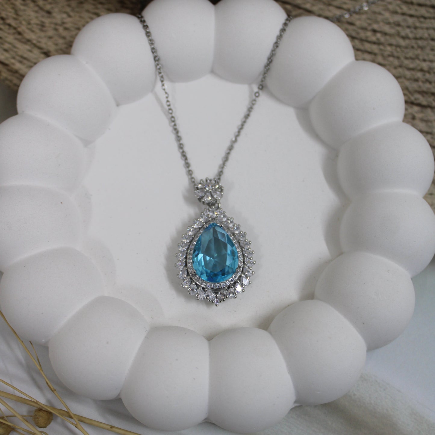 Necklace with a blue teardrop pendant on a white spherical object