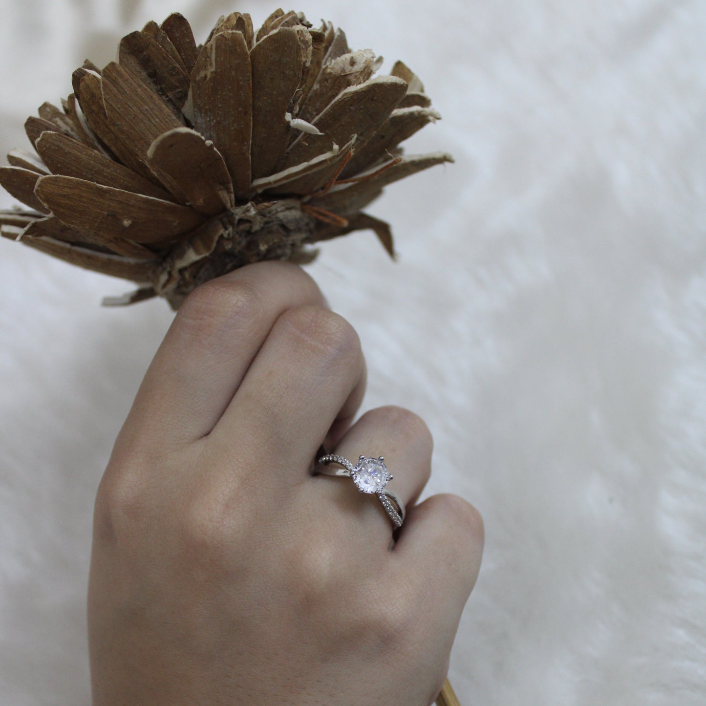 Hand holding a dried flower with a diamond ring on a white background