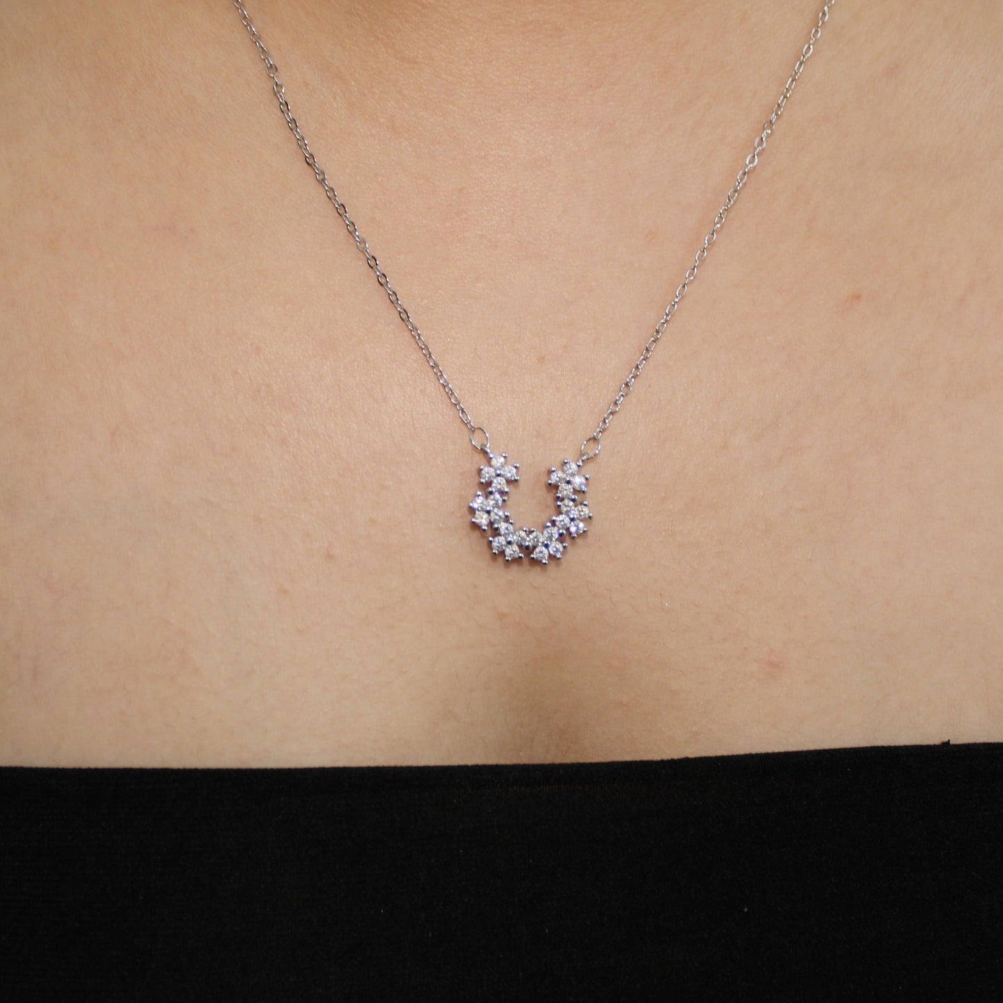 Silver necklace with a small pendant on a person's neck against a neutral background
