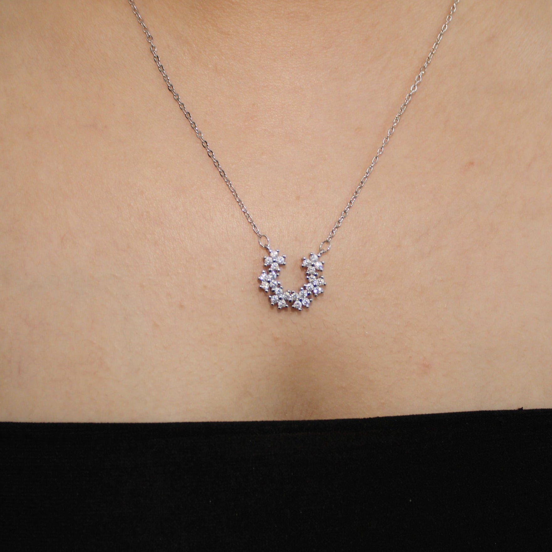 Silver necklace with a small pendant on a person's neck against a neutral background