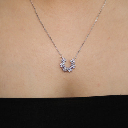 Silver necklace with a small pendant on a person's neck against a neutral background