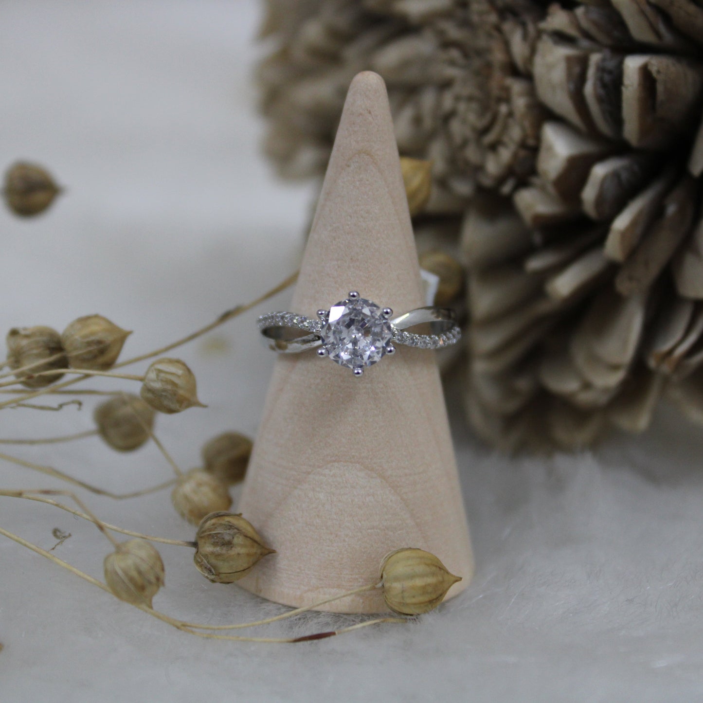 Silver ring on a wooden cone with dried plants and pinecones in the background