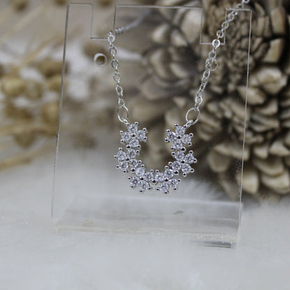 Silver necklace on a clear stand with decorative elements in the background