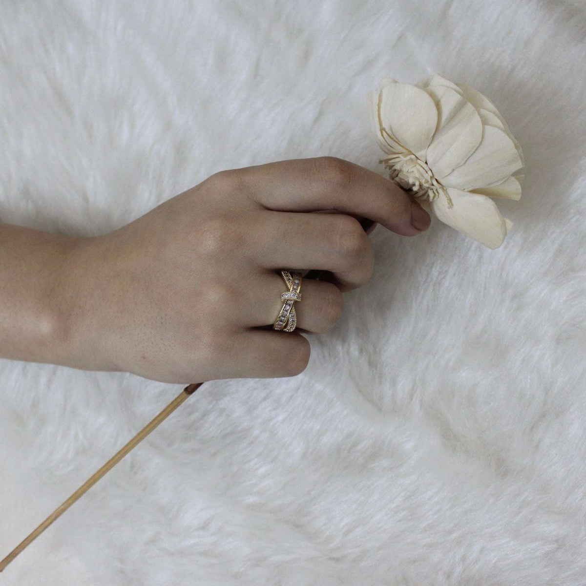Hand with a ring holding a small white flower on a textured white surface