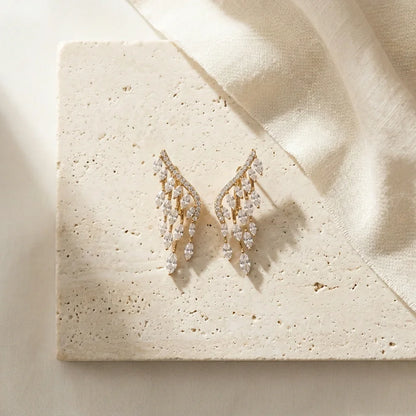 Elegant gold drop earrings with sparkling diamond-like stones on textured stone surface