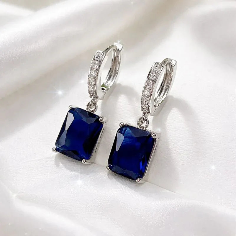 Elegant blue gemstone drop earrings with crystal accents on white fabric