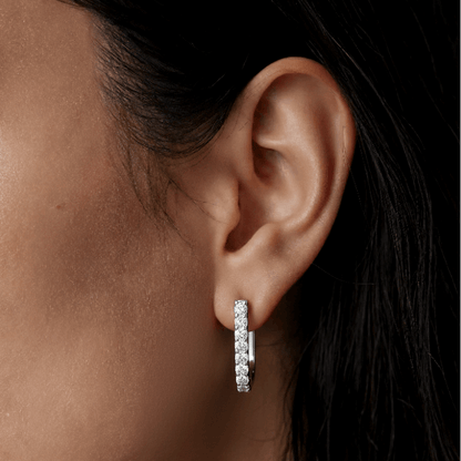 Close-up of an ear wearing a diamond earring with a neutral background