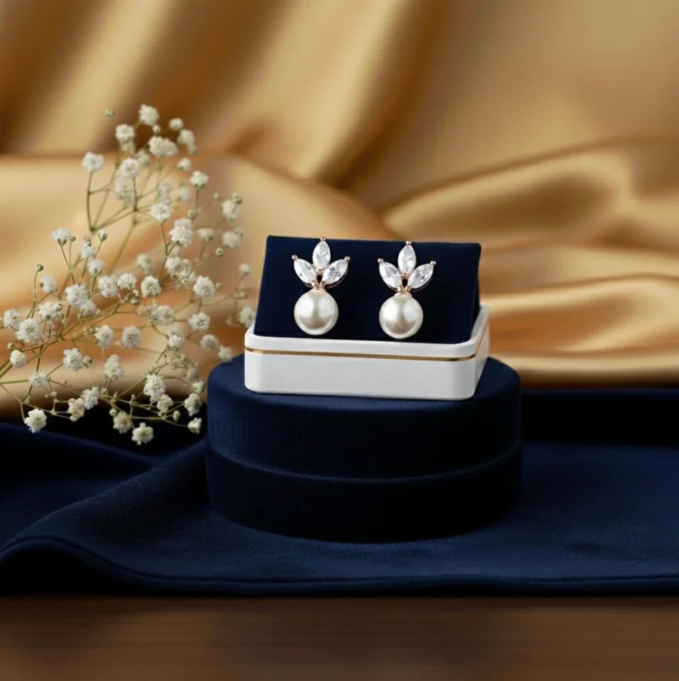 Elegant pearl earrings with crystal accents, displayed in a navy velvet box on a golden silk backdrop.