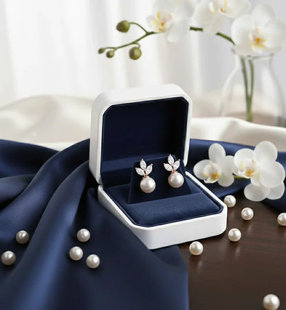 Elegant pearl earrings with diamond accents in a navy velvet box, surrounded by white orchids and loose pearls