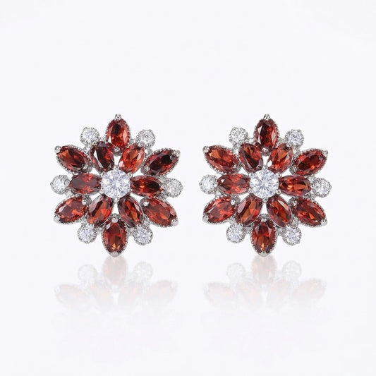 Pair of ruby red flower-shaped earrings with gemstones on a white background
